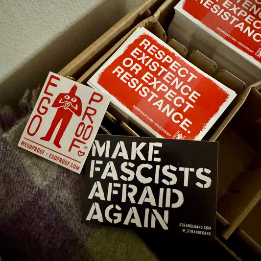 Free Stickers featuring bold messages like “RESPECT EXISTENCE OR EXPECT RESISTANCE” and “MAKE FASCISTS AFRAID AGAIN,” laid over cardboard, embodying voices of empowerment and mental health advocacy.