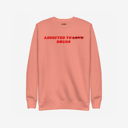 The Addicted To Love / Drugs Sweatshirt EU features bold red text on a salmon-pink crewneck, humorously striking through LOVE to highlight DRUGS, embodying Egoproof’s candid mental health messaging.