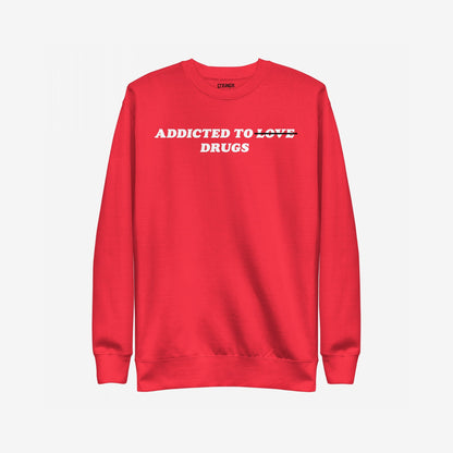 Addicted To Love / Drugs Sweatshirt EU: A red crewneck with bold text humorously altering Addicted to Love to Drugs, embodying candid mental health expression. Features a subtle label at the back neckline.