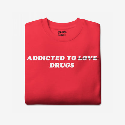 Addicted To Love / Drugs Sweatshirt EU featuring a red crew-neck with crossed-out LOVE and DRUGS below. This unisex piece combines dark humor and honesty, ideal for self-expression and mental health awareness.