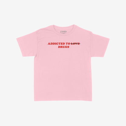 Addicted To Love / Drugs Women's Baby Tee in pink with bold text "Addicted to Drugs" and crossed out "Love" on front, fitted Y2K style shirt.