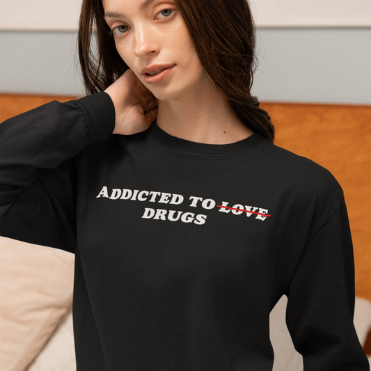 Model wearing black Addicted To Love / Drugs Long Sleeve T-shirt with text “Addicted to Drugs” in casual indoor setting.