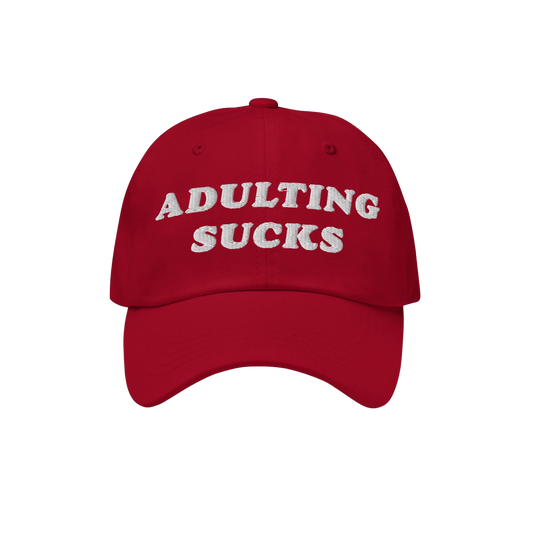 Red baseball-style cap with ADULTING SUCKS embroidered in white on front, representing Egoproof's relatable, bold apparel. Id