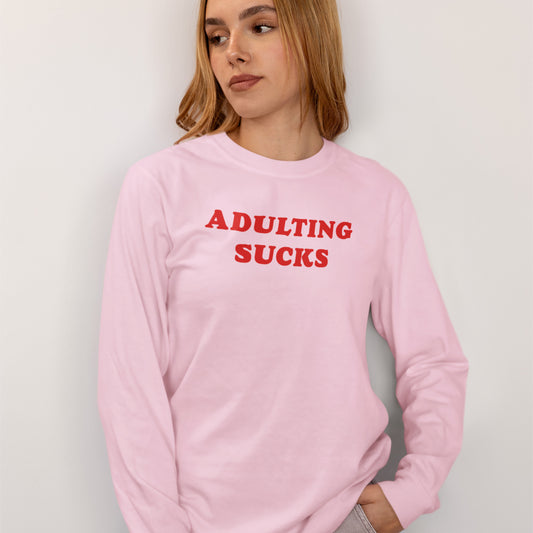 Adulting Sucks Long Sleeve T-shirt in pink with bold red text, modeled by a woman, casual unisex fit, comfortable and relatable design.