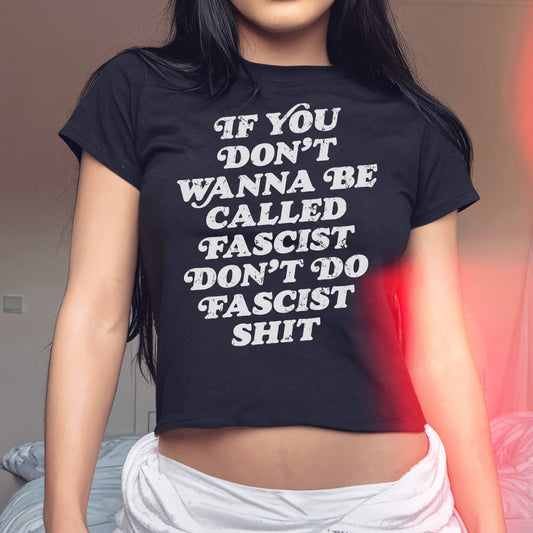 Anti-Fascist Women's Baby Tee featuring bold white text on a black, short-sleeved crop top. The shirt empowers wearers with its unapologetic statement, If you don’t wanna be called fascist, don’t do fascist shit.