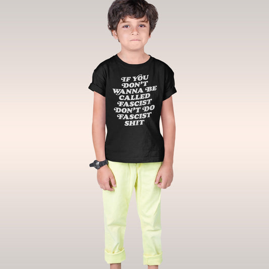 Young boy wearing the Anti-Fascist T-shirt displaying a bold message against fascism, paired with pale yellow pants and a wri