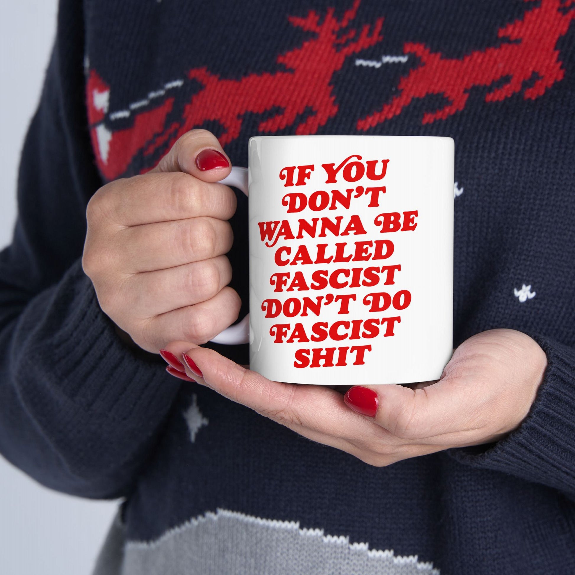 A person with red-painted nails holds an Anti-Fascist Mug featuring bold red text: “If you don’t wanna be called fascist don’t do fascist shit,” blending vintage style with a powerful message.