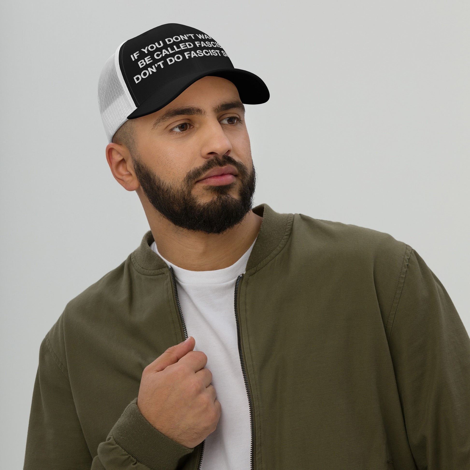 Young man wearing the Anti-Fascist Hat featuring the bold statement, IF YOU DON’T WANT TO BE CALLED FASCIST DON’T DO FASCIST SHIT, paired with an olive-green jacket, embodying resistance and awareness.