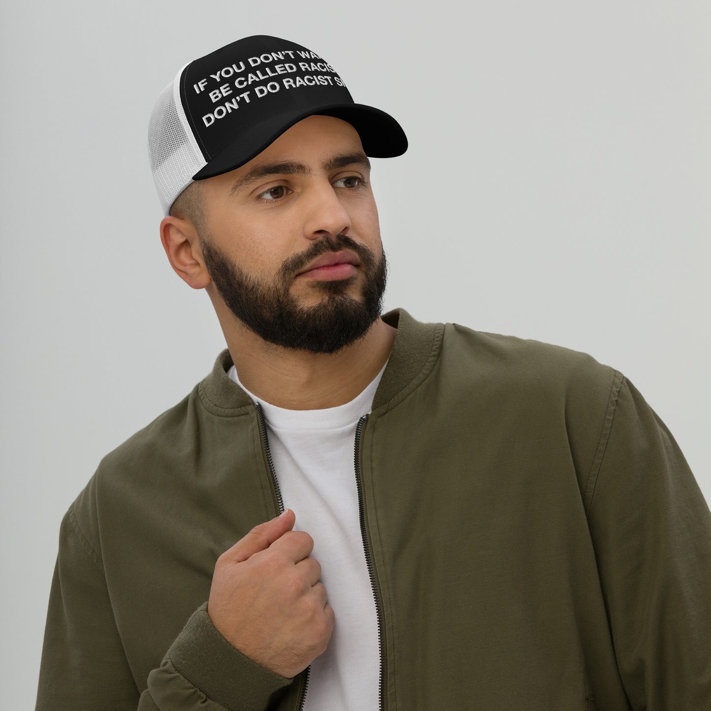 Anti-Racist Hat EU: Bearded man wears a trucker cap with bold anti-racist slogan, paired with an olive jacket. This hat makes a powerful statement against racism, embodying style and social awareness.