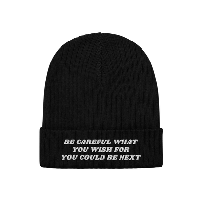 Black rib-knit beanie with folded-cuff, featuring white embroidered text BE CAREFUL WHAT YOU WISH FOR YOU COULD BE NEXT on fr