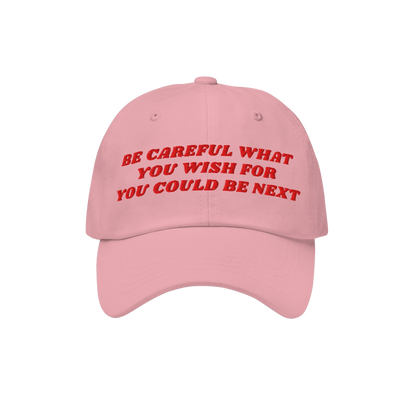 Be Careful Hat featuring red embroidered text 'BE CAREFUL WHAT YOU WISH FOR YOU COULD BE NEXT' on a pink baseball cap, embody