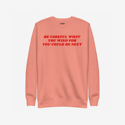 Coral-pink Be Careful Sweatshirt EU with bold red anti-fascist message BE CAREFUL WHAT YOU WISH FOR YOU COULD BE NEXT across the chest, featuring a small inside collar label.
