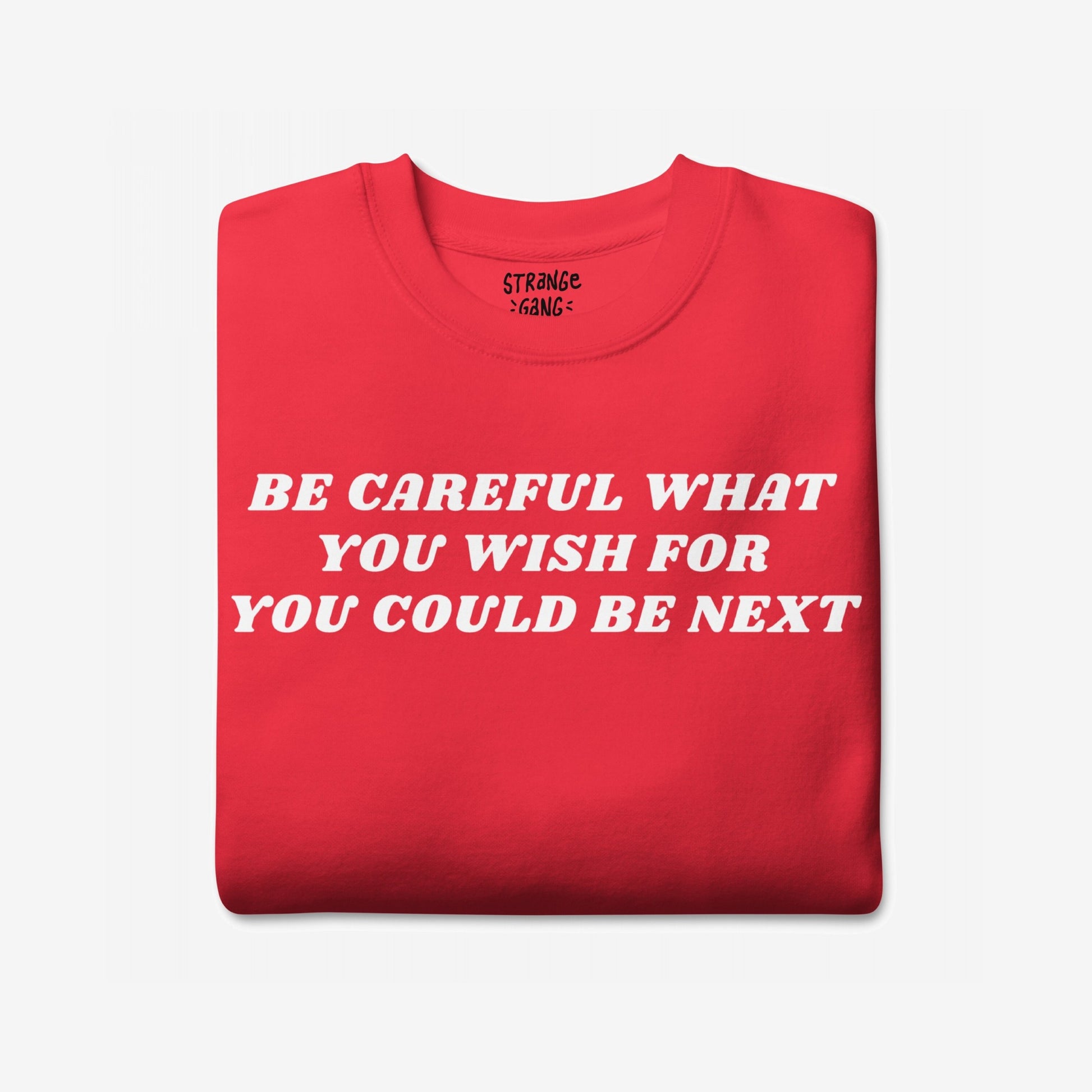 The Be Careful Sweatshirt EU displays bold white text warning BE CAREFUL WHAT YOU WISH FOR YOU COULD BE NEXT on a folded red garment, embodying activism and resistance.