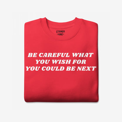 The Be Careful Sweatshirt EU displays bold white text warning BE CAREFUL WHAT YOU WISH FOR YOU COULD BE NEXT on a folded red garment, embodying activism and resistance.
