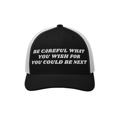 Black-and-white trucker-style baseball cap with BE CAREFUL WHAT YOU WISH FOR YOU COULD BE NEXT embroidered on the front. The 