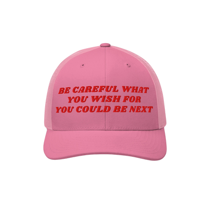 Be Careful Hat: A pink trucker-style cap with bold red embroidery stating “BE CAREFUL WHAT YOU WISH FOR YOU COULD BE NEXT,�