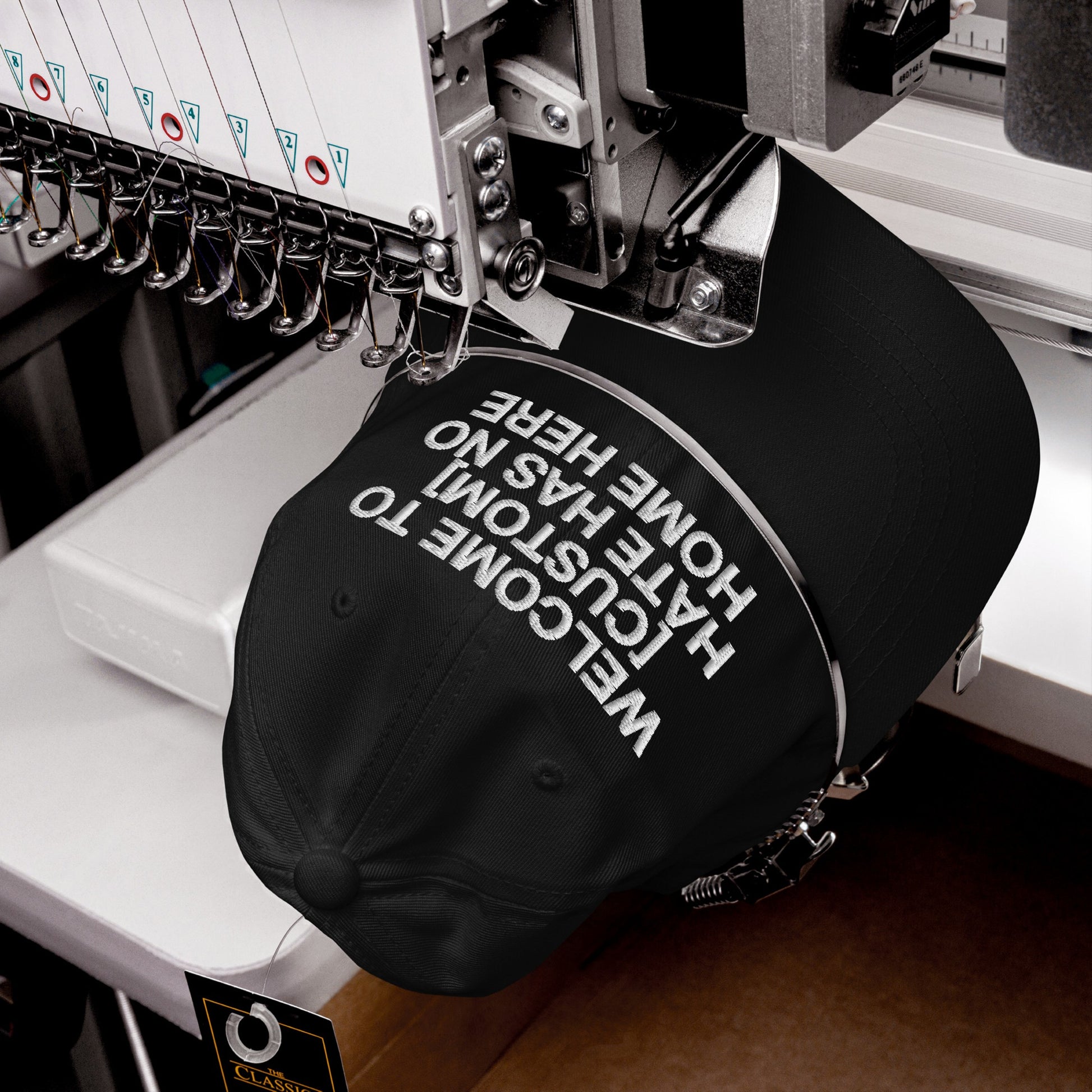 Custom Hate Has No Home Here Dad Hat in black being embroidered with bold white text on adjustable chino cotton cap