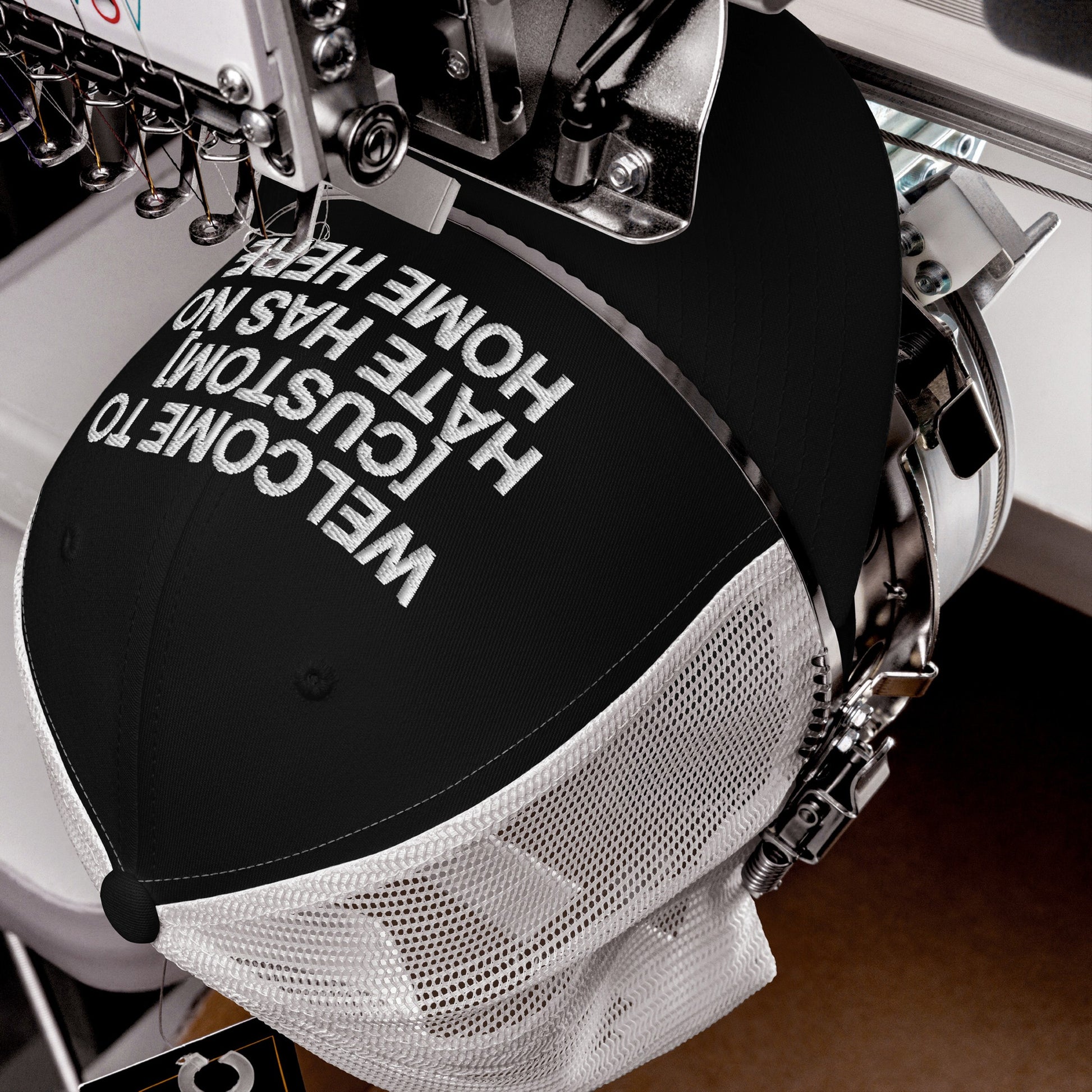 Custom Hate Has No Home Here Trucker Hat being embroidered with bold white text on a black and white mesh trucker cap