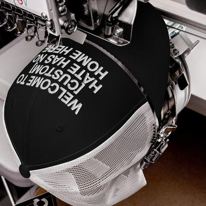 Custom Hate Has No Home Here Trucker Hat being embroidered with bold white text on a black and white mesh trucker cap