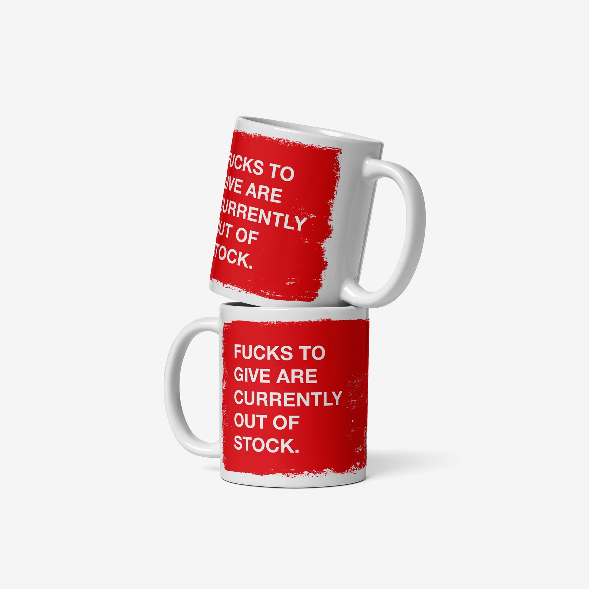 Two white ceramic Fucks To Give Mugs stacked, each with a red rectangle and bold text: “FUCKS TO GIVE ARE CURRENTLY OUT OF STOCK.” A bold statement piece for your emotional inventory.
