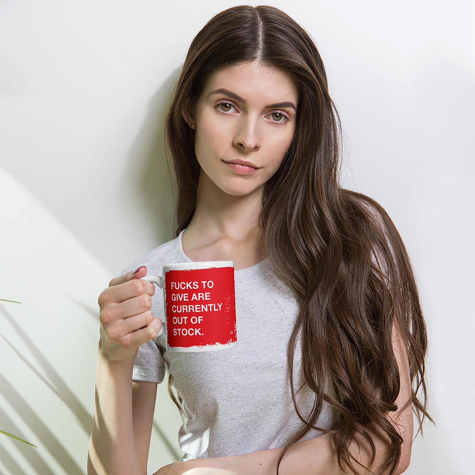 Young woman with long dark hair holds a white ceramic mug featuring the phrase “Fucks to give are currently out of stock” in red, symbolizing a bold emotional statement for Egoproof's mental health-focused collection.