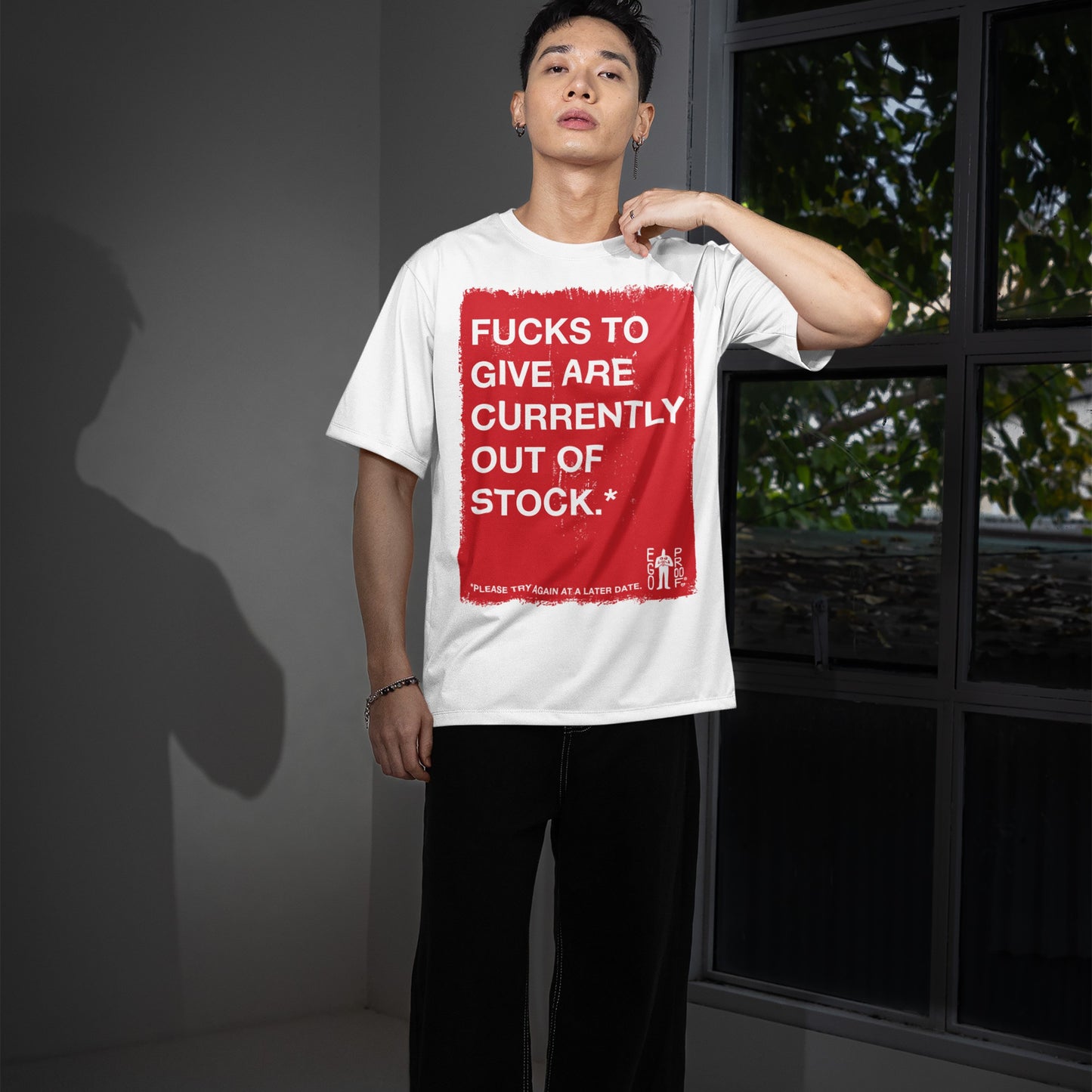 Young man wearing Fucks To Give T-shirt with bold, honest message. Casual style, minimalism reflected in loose black pants and bracelet, embodying Egoproof's artful, candid approach to mental health awareness.
