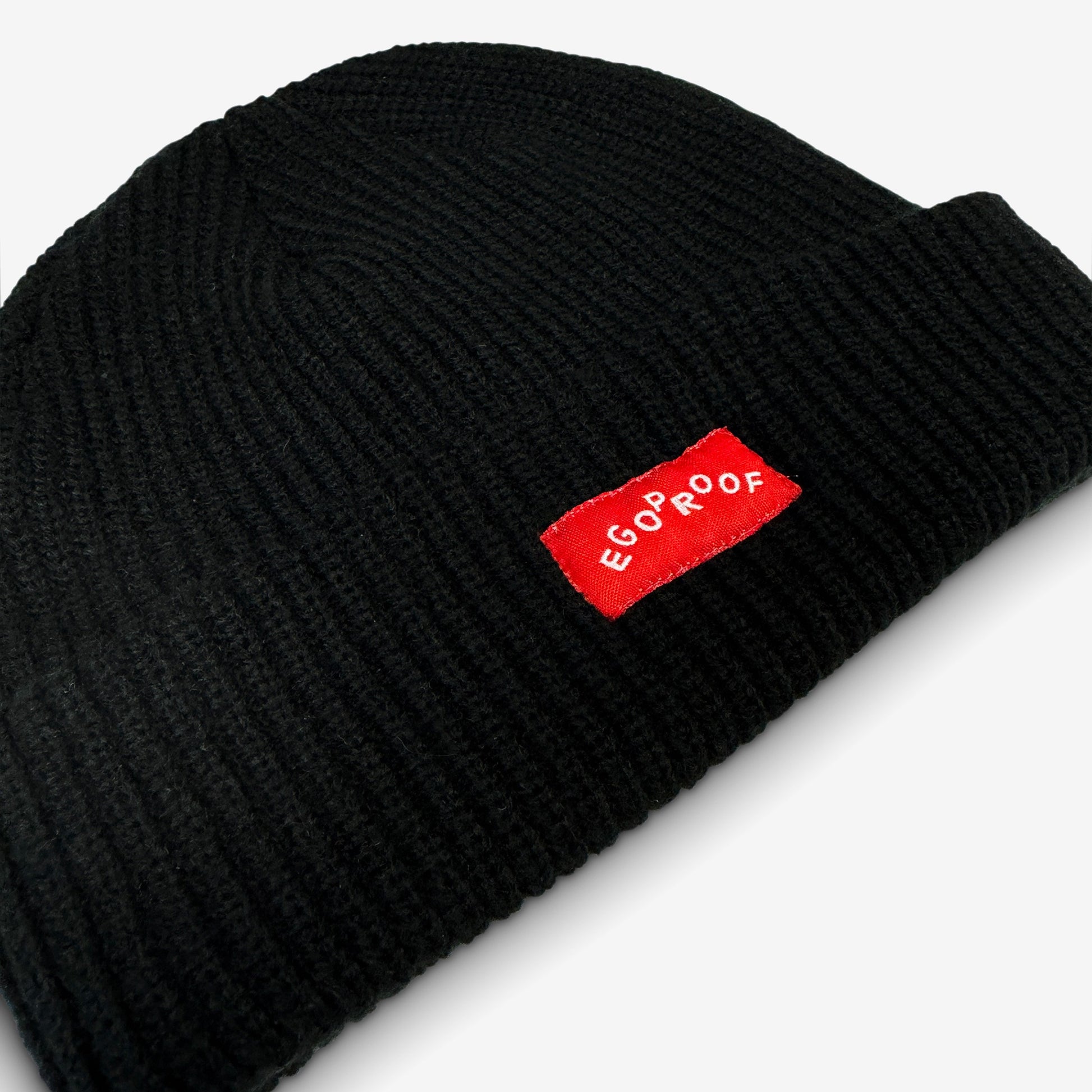 Go Fish Beanie with a red woven EGOPROOF label, featuring a wide ribbed cable knit design, exemplifying warmth and understated style.