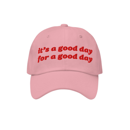 Good Day Hat features a light-pink dad hat with red embroidered text, it's a good day for a good day, promoting positivity an