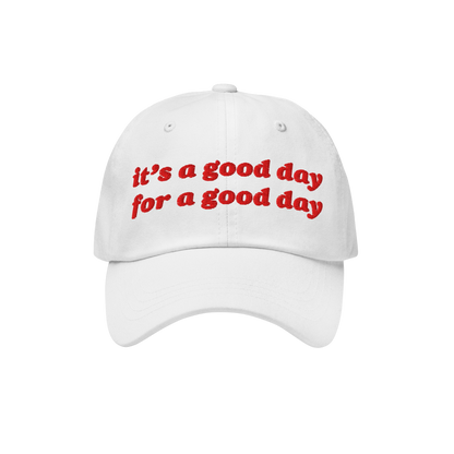 White baseball-style cap with red embroidered text reading “it’s a good day for a good day.” The Good Day Hat embodies 