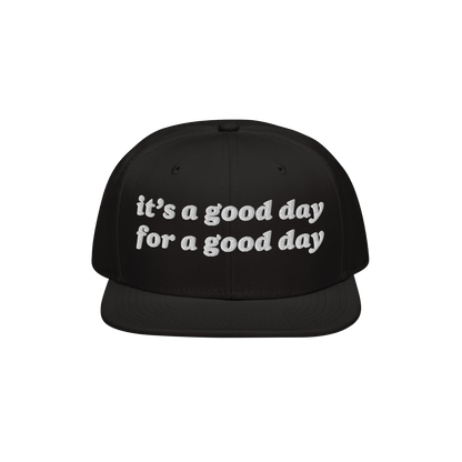 Black flat-brimmed snapback hat with white embroidered text: “it’s a good day for a good day.” The Good Day Hat promote
