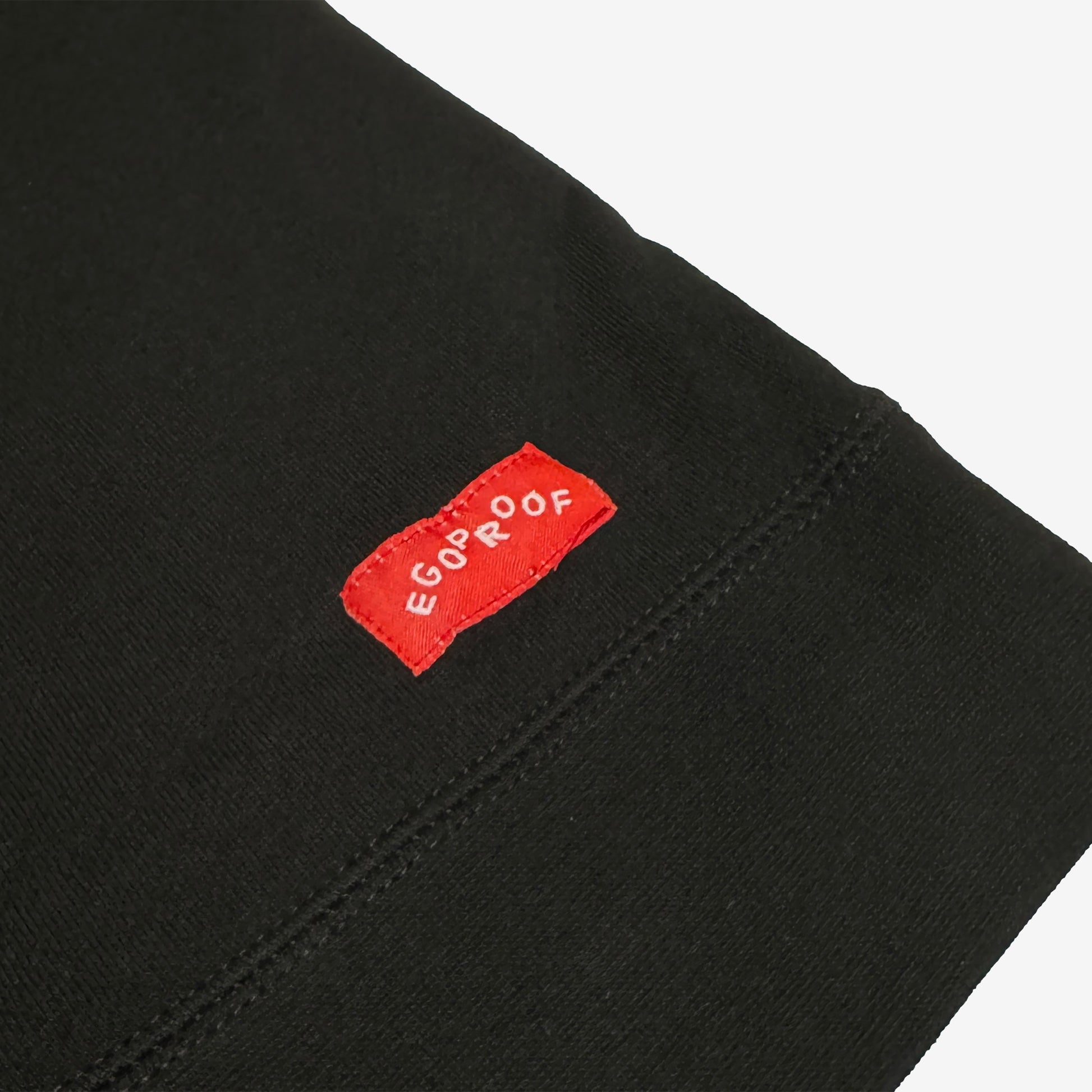 The Good Day Sweatshirt features a close-up of its hem with a small red woven EGOPROOF label, embodying subtle positivity in line with Egoproof’s mental health-focused apparel ethos.