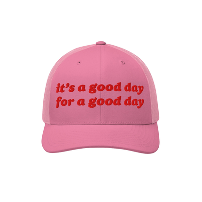 Pink trucker-style baseball cap featuring red embroidered text: “it’s a good day for a good day.” The Good Day Hat embo
