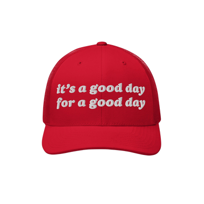 Red trucker-style baseball cap with white embroidered text reading “it’s a good day for a good day.” The Good Day Hat p