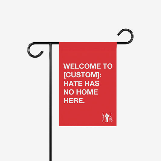 Custom Hate Has No Home Here Garden Flag with bold white text on a small red flag, hanging from a black metal stand. Personalize with a location name, featuring the wordmark “EGO PROOF.”