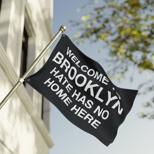 Custom Hate Has No Home Here Flag displayed outside a building, showcasing bold white text on a black banner. The flag advocates unity and inclusion, customizable with different city names.