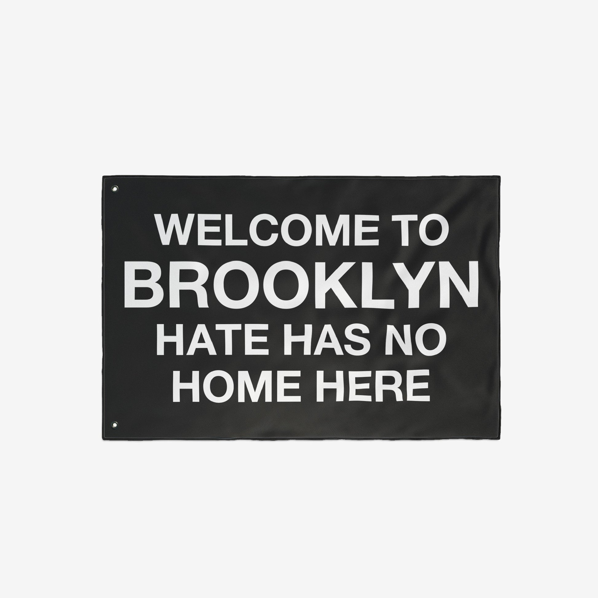 Custom Hate Has No Home Here Flag featuring bold, white text on a black background. Includes metal grommets for hanging. Ideal for showcasing unity and acceptance in various settings.
