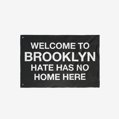 Custom Hate Has No Home Here Flag featuring bold, white text on a black background. Includes metal grommets for hanging. Ideal for showcasing unity and acceptance in various settings.