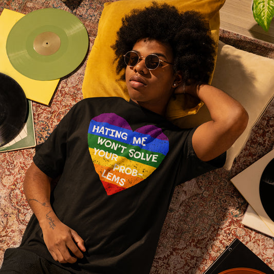 Person wearing No LGBTQ Hate T-shirt with rainbow heart and “Hating Me Won’t Solve Your Problems” text lying on floor near vinyl records
