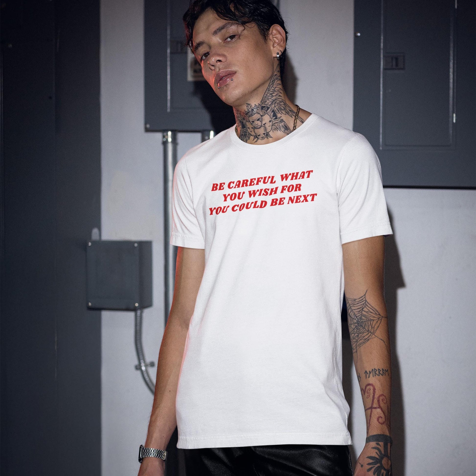 Young man wearing white Be Careful T-shirt with red text warning in urban setting, showcasing bold minimalism style.