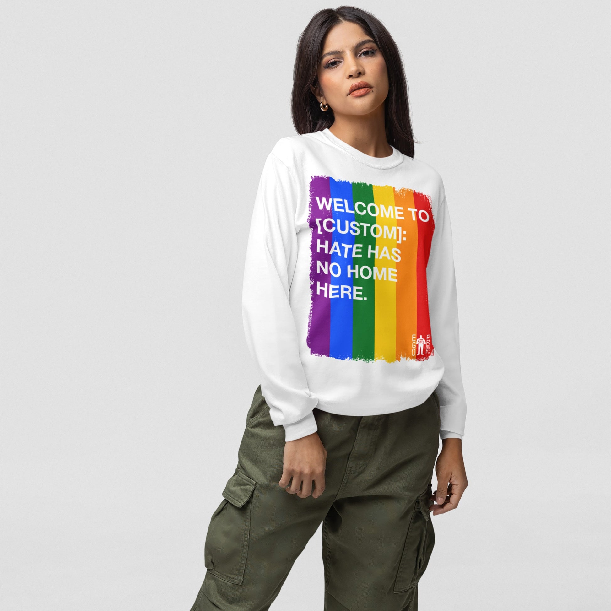 Custom Hate Has No Home Here Pride Long Sleeve T-shirt featuring a brush-stroked rainbow with customizable city or community name, worn by a young woman, promoting LGBTQ+ inclusivity and comfort.
