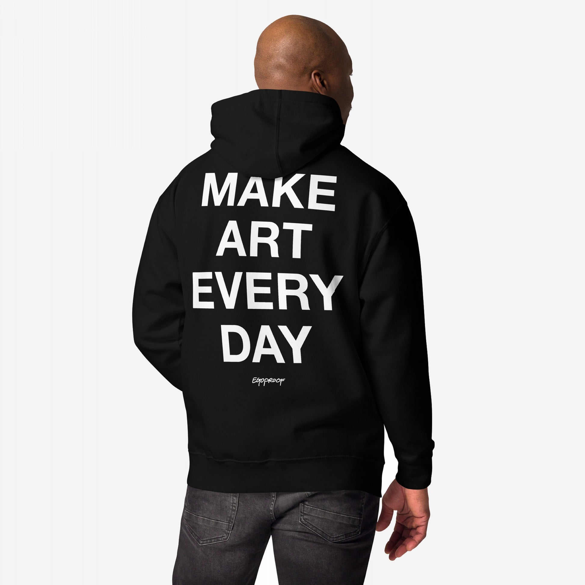 Person wearing Make Art Every Day Hoodie EU with bold white slogan and logo on back, against a plain background. The hoodie symbolizes creative resilience and everyday artistic expression.