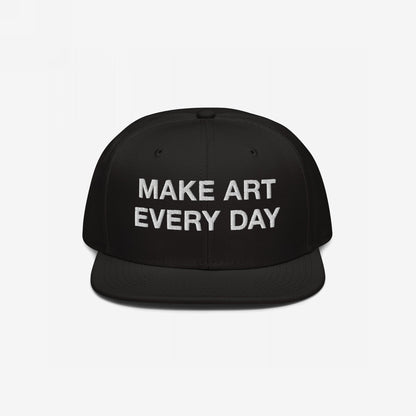 Black flat-brim snapback cap titled Make Art Every Day featuring bold white embroidered message, encouraging creativity and persistence. Includes adjustable fit and additional back embroidery for versatile, everyday wear.
