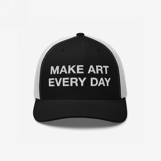 The Make Art Every Day Hat features a black-and-white mesh-back design with a black front panel, embroidered with “MAKE ART EVERY DAY” in white letters, embodying creativity and resilience.