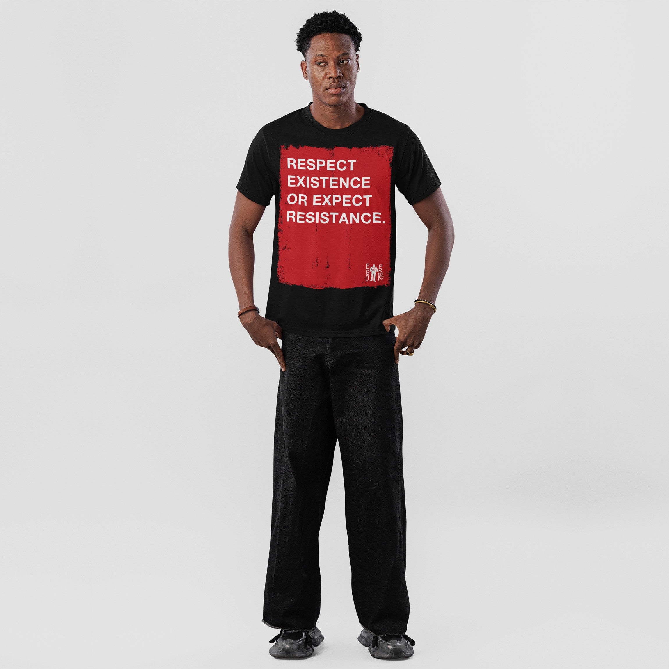 Young man in a Respect Existence T-shirt, featuring a bold red square with a powerful slogan. He pairs it with loose black jeans and sneakers, embodying resistance and awareness.