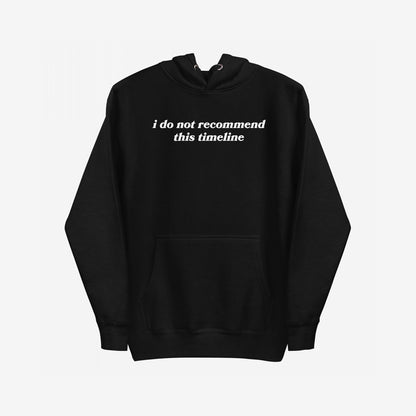 Timeline Hoodie EU: A black pullover with a kangaroo pocket, featuring the phrase i do not recommend this timeline in white serif lettering across the chest. Ideal for those feeling overwhelmed.