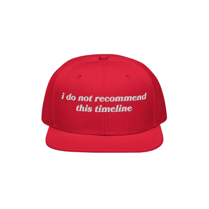 Red snapback cap with flat brim featuring white embroidered text reading “i do not recommend this timeline.” Ideal for ir