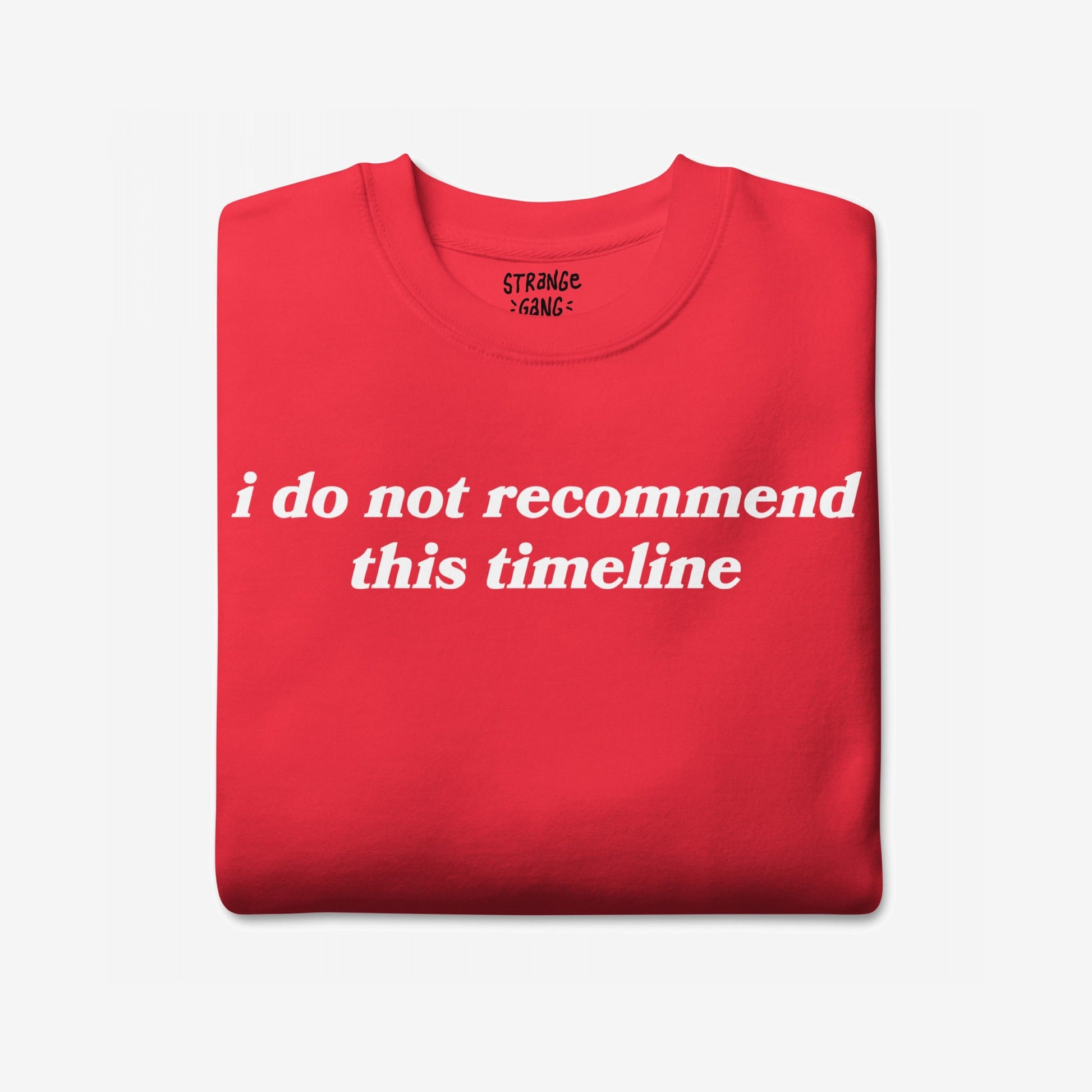 Folded red sweatshirt displaying bold white text: “i do not recommend this timeline.” Aimed at doomsday scrollers, the Timeline Sweatshirt EU offers a sarcastic take on modern life's absurdity.