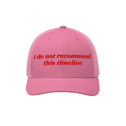 Pink mesh-back trucker cap with red embroidery reading “i do not recommend this timeline.” The Timeline Hat blends retro 