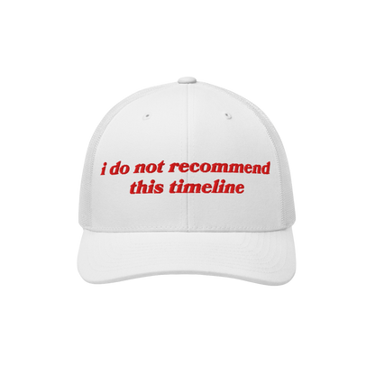 White mesh-back trucker cap with a curved brim featuring bold red embroidery: “I Do Not Recommend This Timeline.” A state
